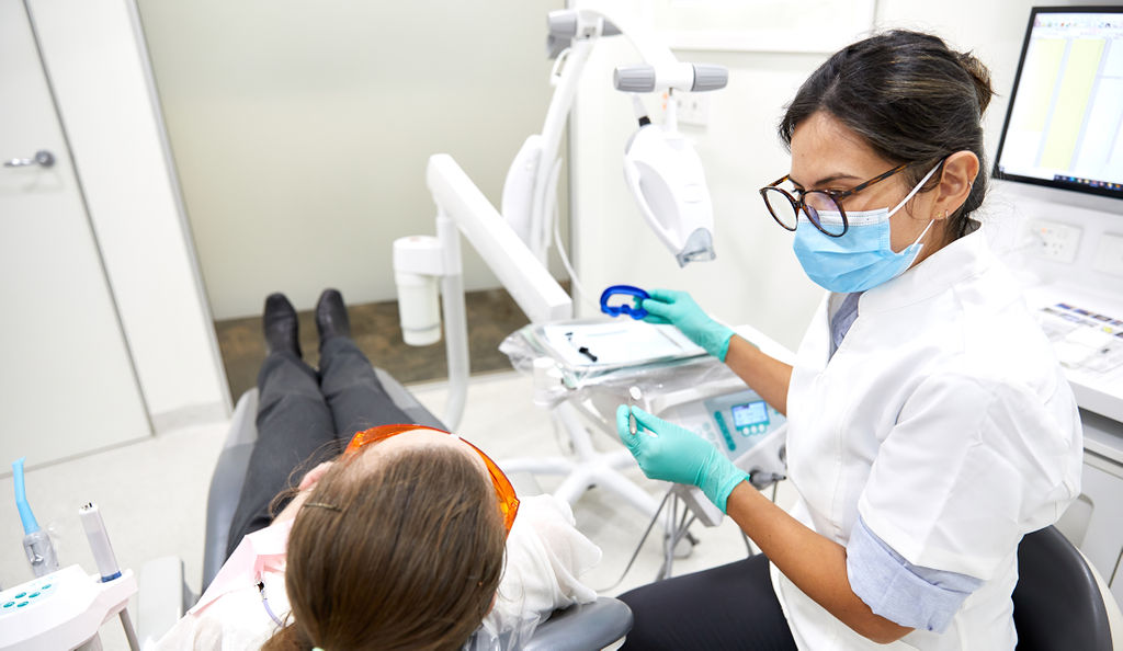 Female dentist wearing glasses and mask in a white shirt working with a patient